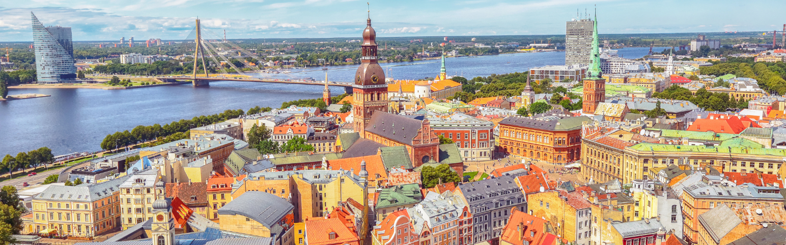 A city skyline with many vibrantly colored buildings of varying heights and shapes. A river is behind the city. 
